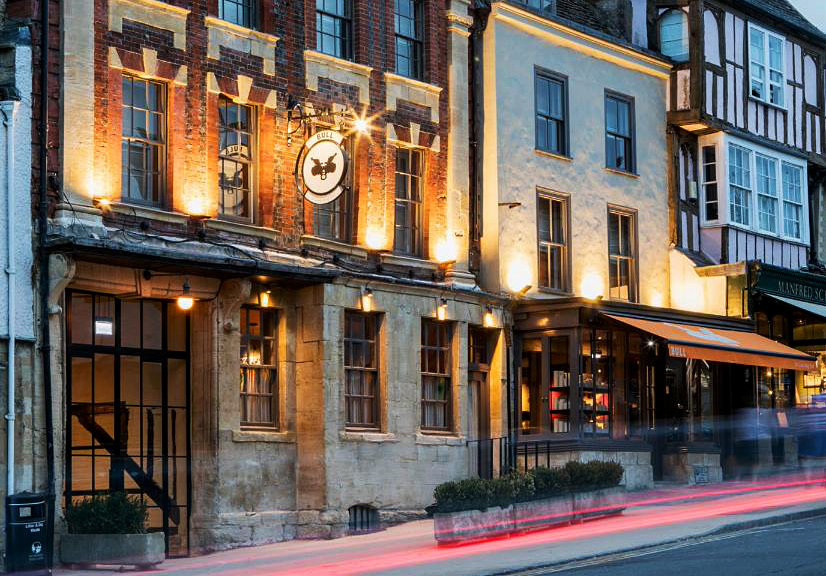 Façade of the Bull pub at night as people and cars stream by