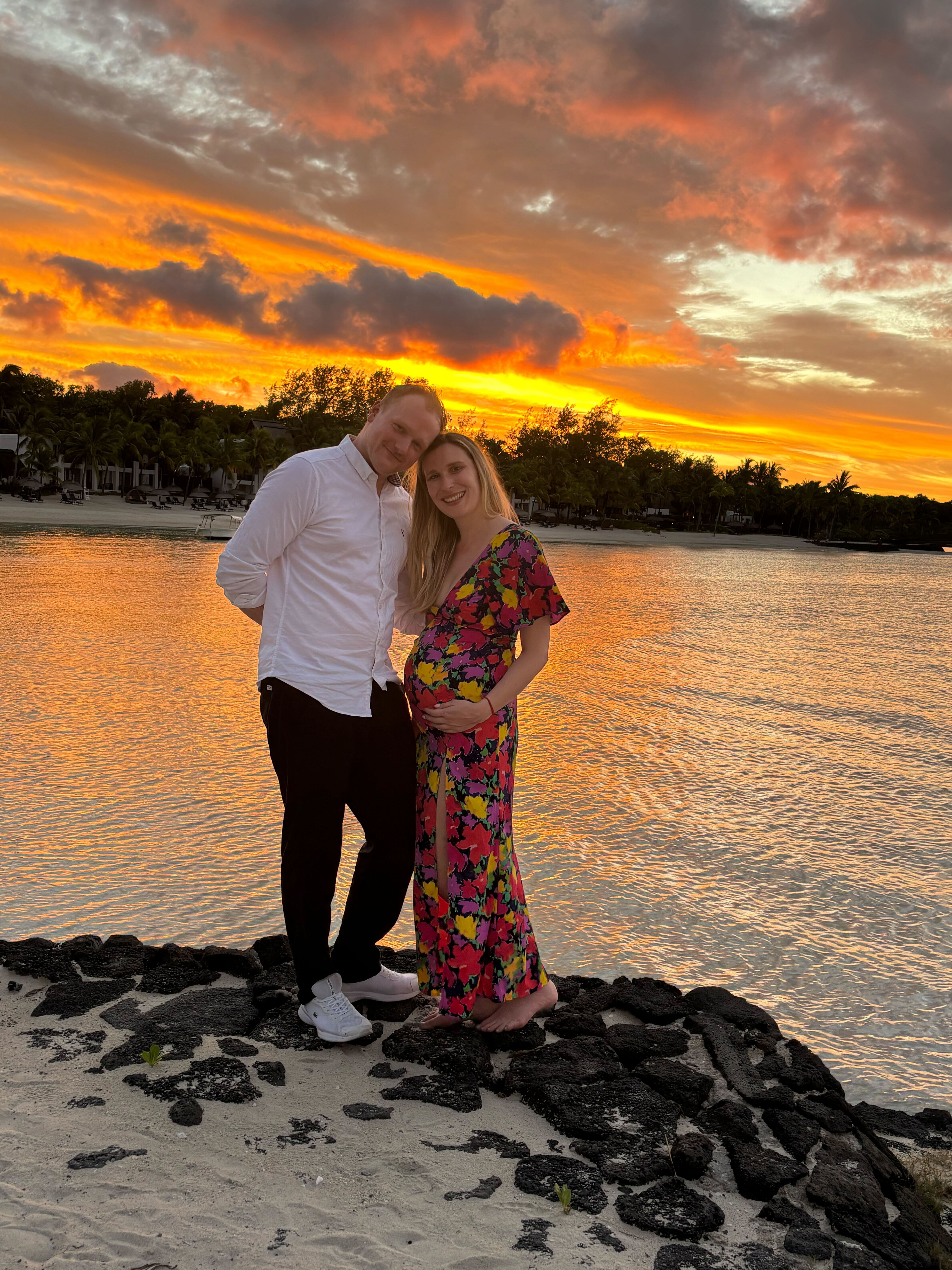 Pregnant woman and man at sunset by the ocean.